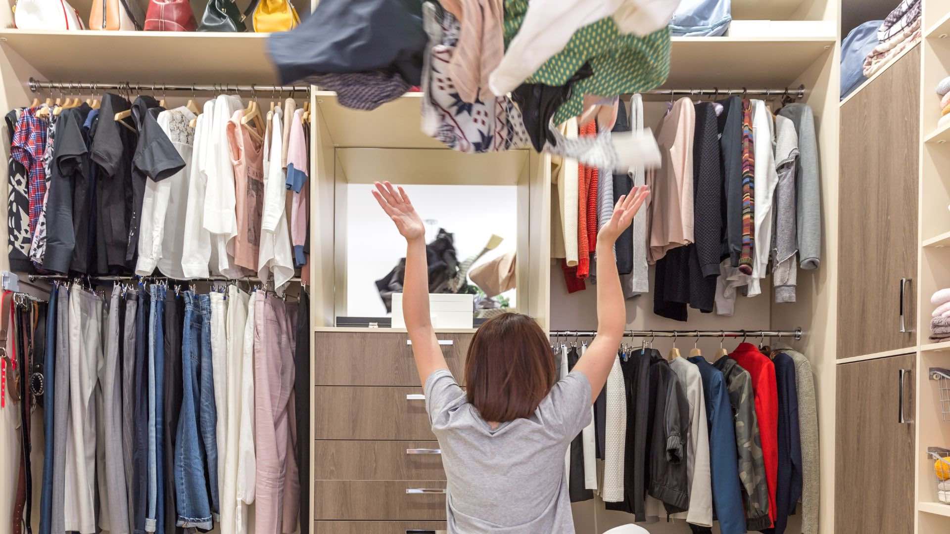 A young women sitting in a closet throwing clothes