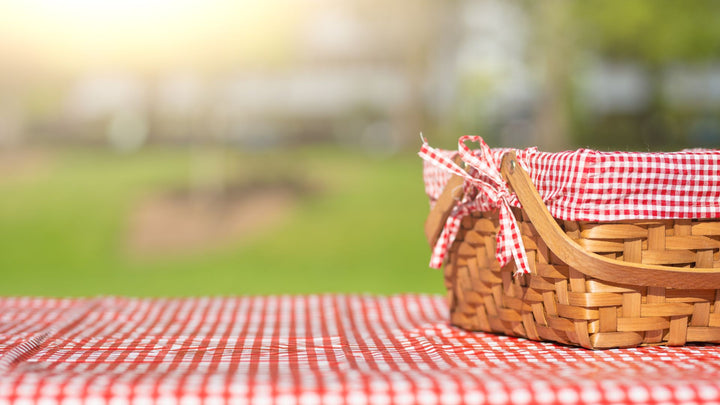 A wicker picnic basket on a red picnic blanket 