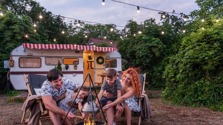 A family outside there RV around a fire with lights hanging above them