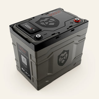 A rugged black and dark gray RV battery with a digital terminal monitor on top and a red positive terminal cap, shown on a light beige background.